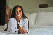 Smiling girl with a BAMWOO bamboo toothbrush lying on a bed in a villa in Bali, Indonesia