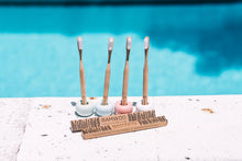 Four BAMWOO bamboo toothbrushes standing upright in ceramic toothbrush holders