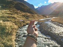 A BAMWOO bamboo toothbrush held in front of a mountain stream on a hiking trip in the Austrian Alps