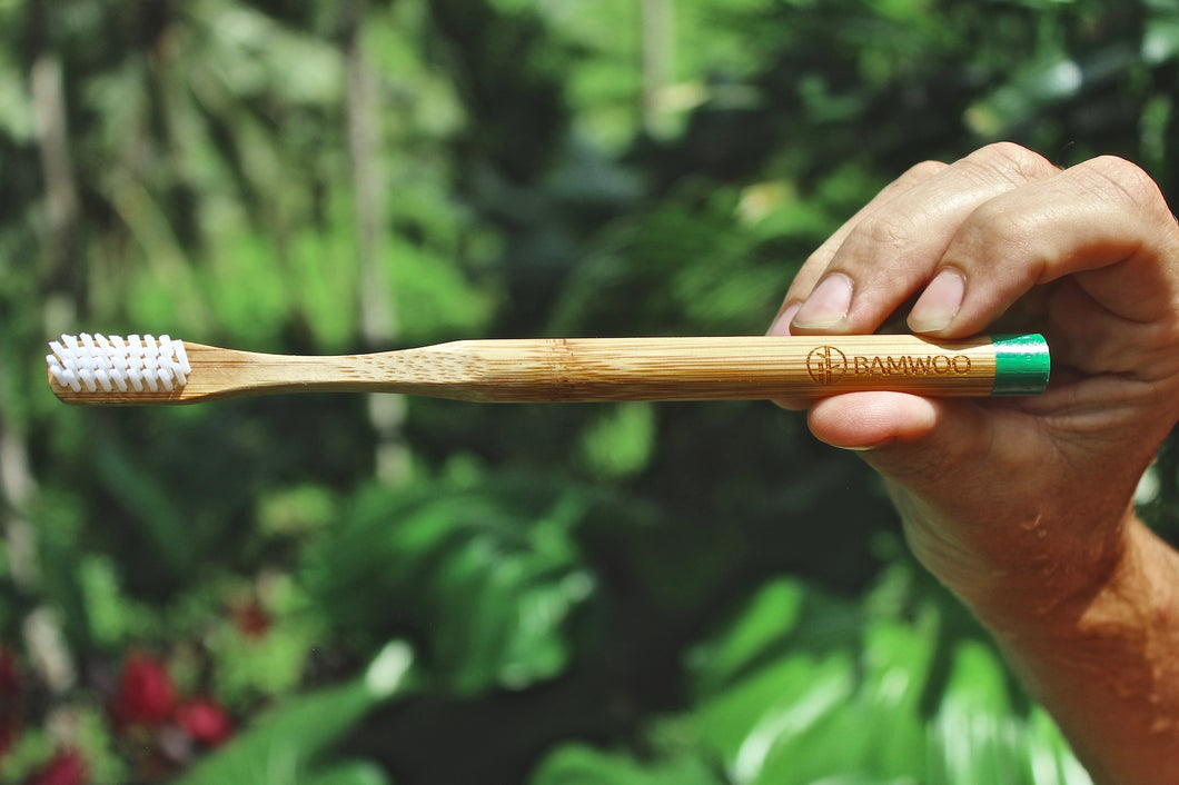 A bamboo toothbrush from BAMWOO held up in front of the jungle in Ubud, Bali